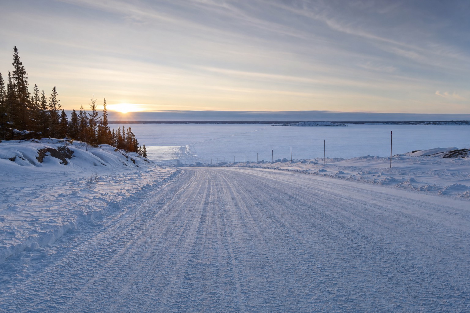 Plowed ice road stretching across frozen Yellowknife Bay toward the far shore under a low winter sun