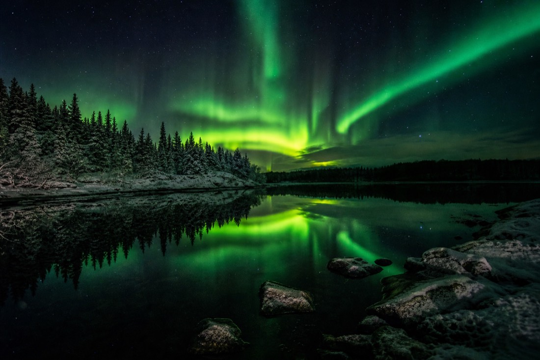 Bright green aurora curtains perfectly mirrored in still dark lake water