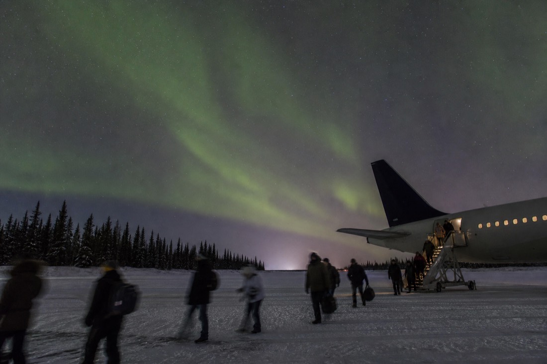 Passengers in winter coats walking across the snowy tarmac from a plane at Yellowknife airport