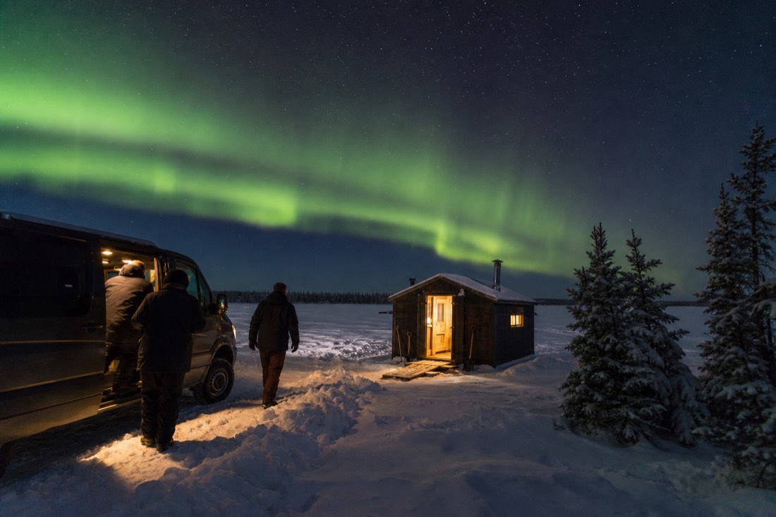 Guests stepping from a heated tour van into a warm wood-lined fishing hut on the frozen lake