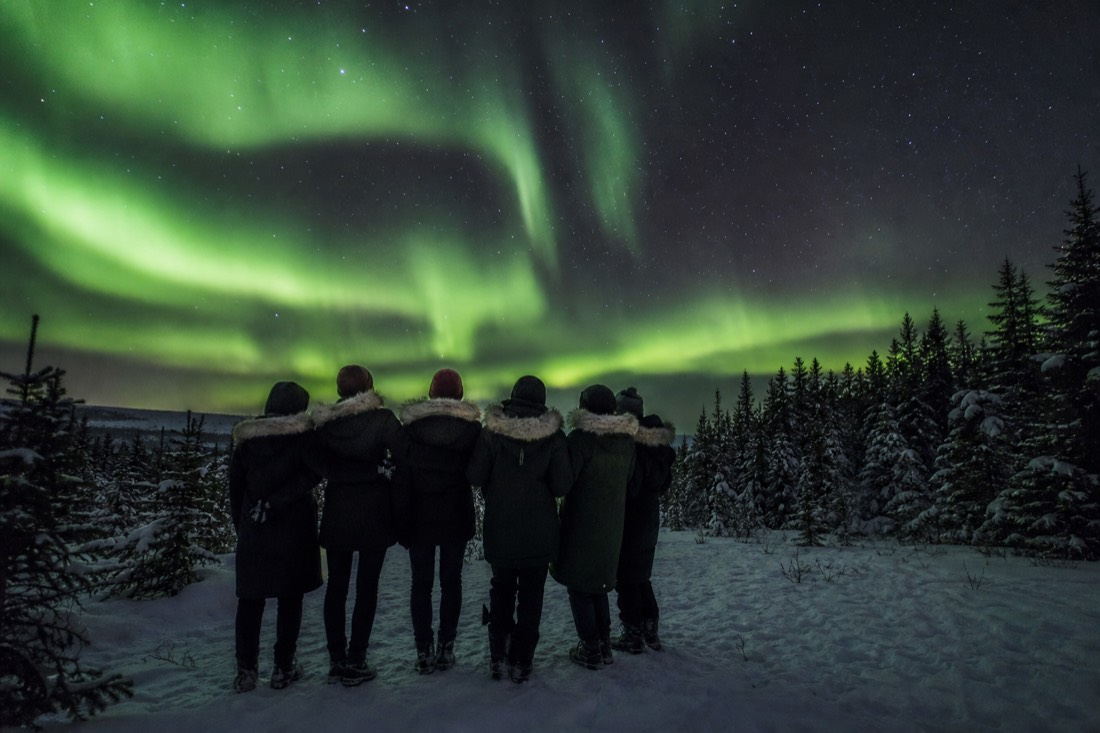 Smiling group in rented arctic parkas under a bright green aurora on a very cold clear night