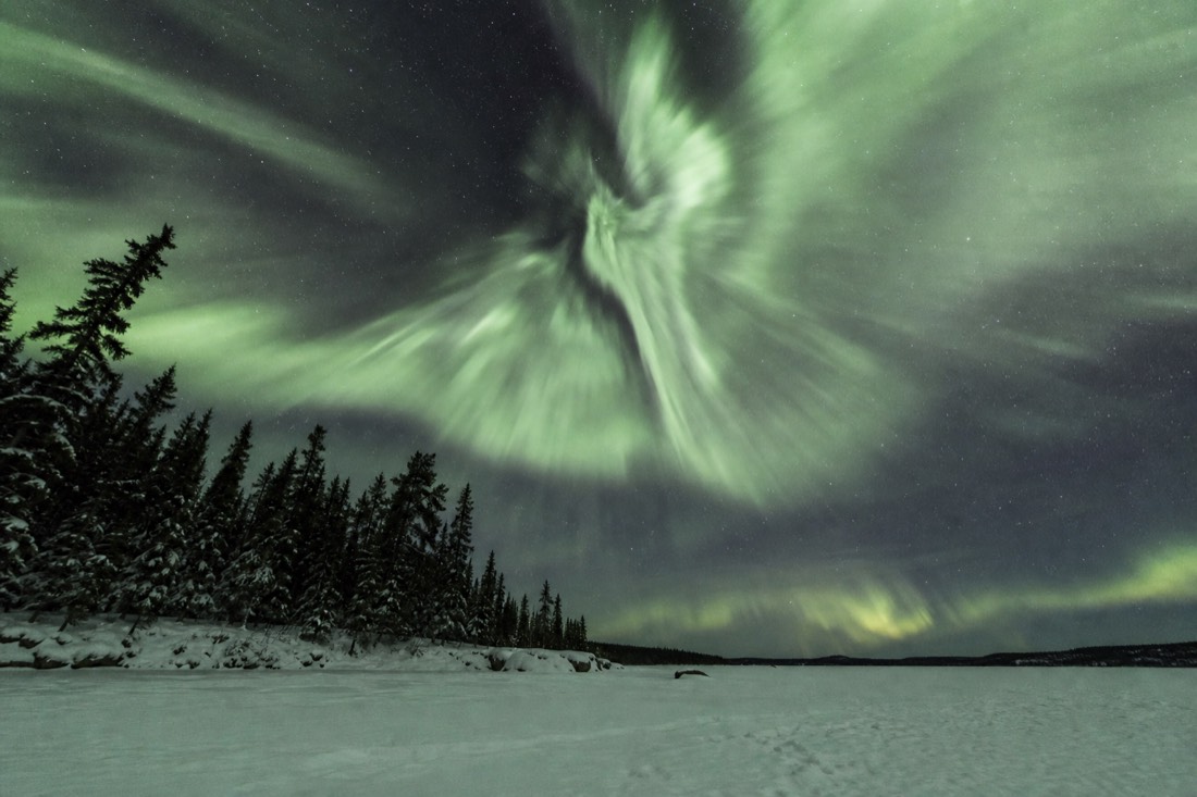 Aurora corona bursting directly overhead above a snow-covered lake outside Yellowknife