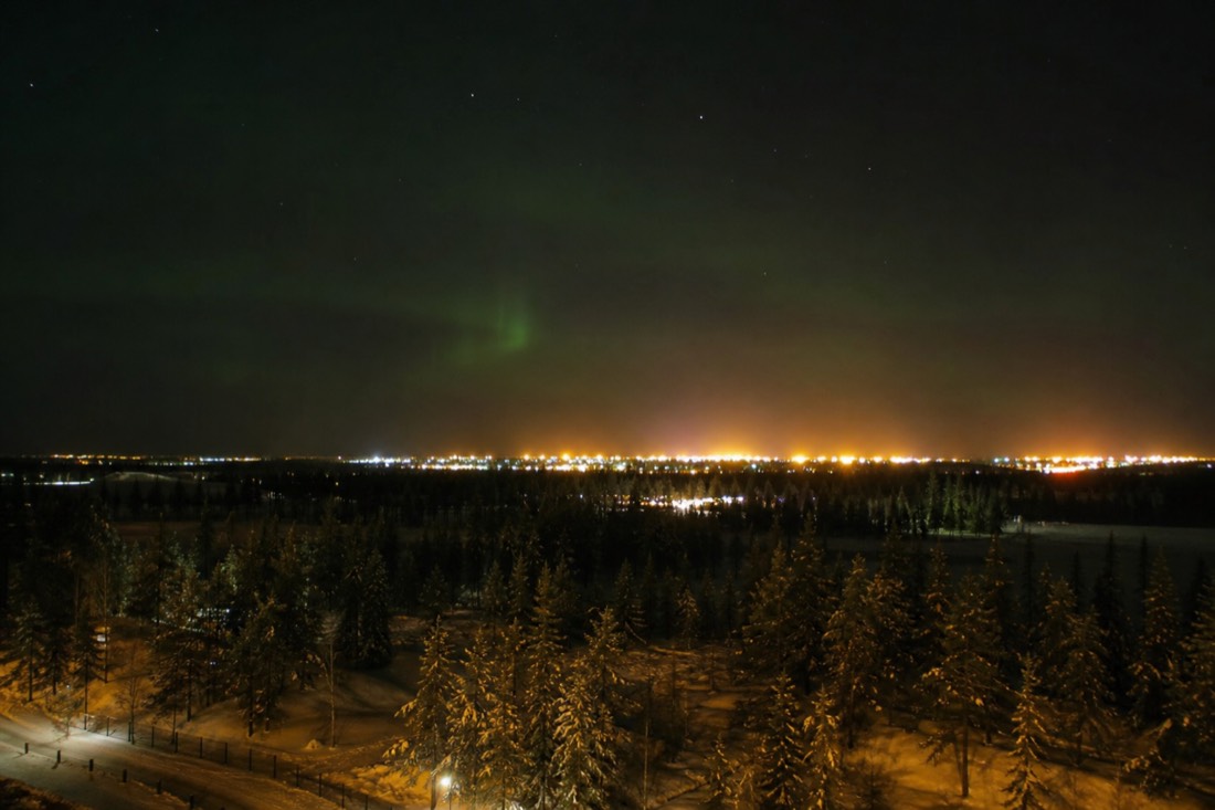 Faint green aurora barely visible above the orange glow of Yellowknife city lights seen from a hotel window