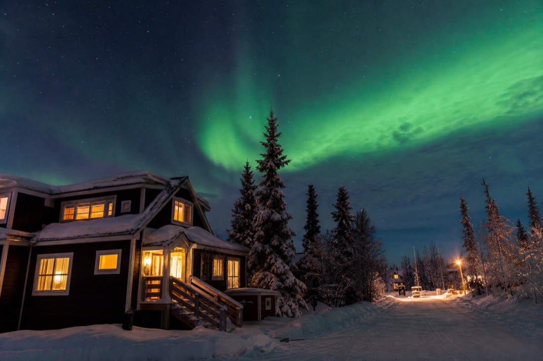 A small guesthouse with warm windows on a snowy Yellowknife side street under a starry winter sky