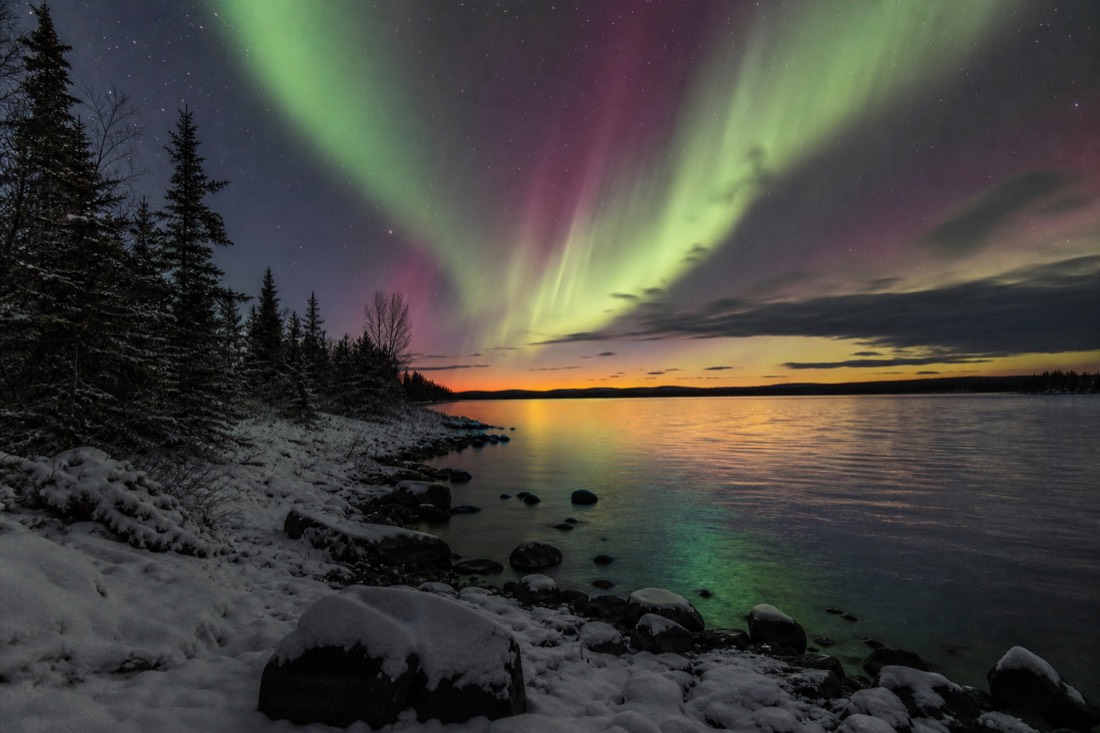 First autumn aurora of the season glowing above a lake at twilight with the horizon still faintly orange