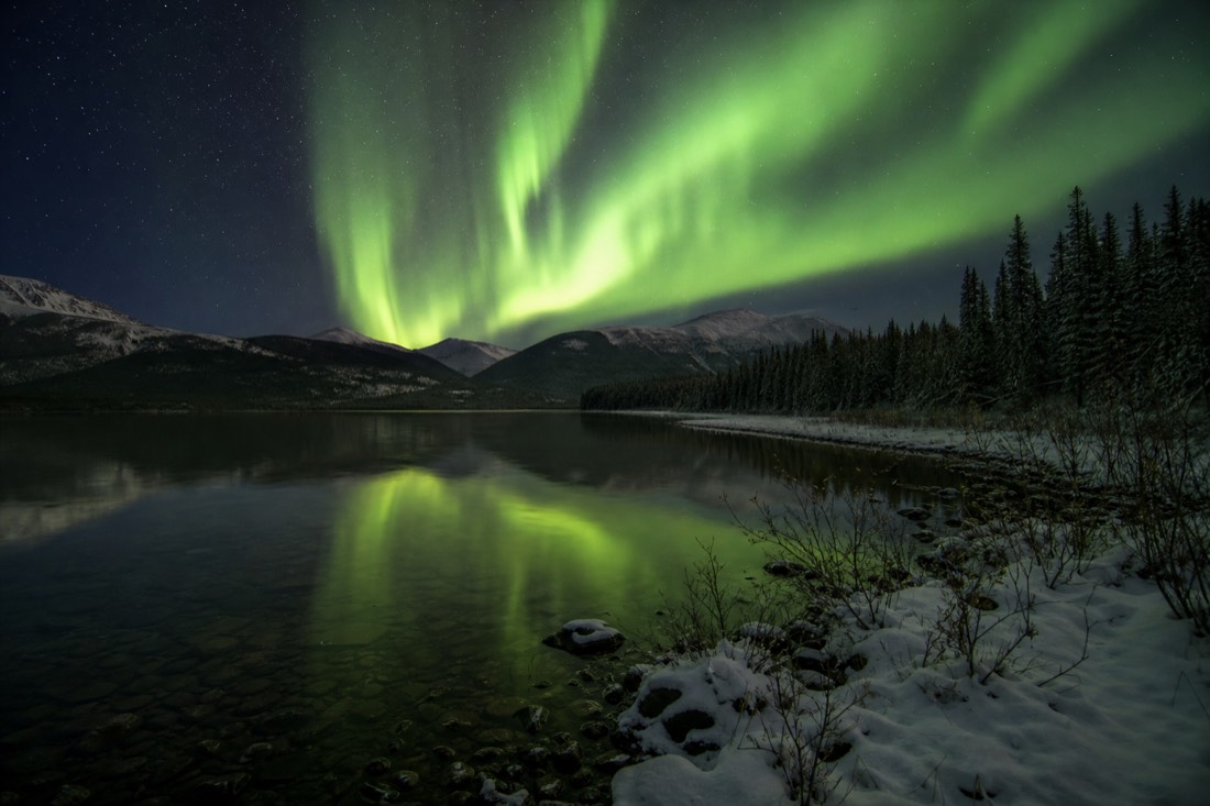 Bright green aurora curtains reflected in the dark open water of a subarctic lake in early autumn