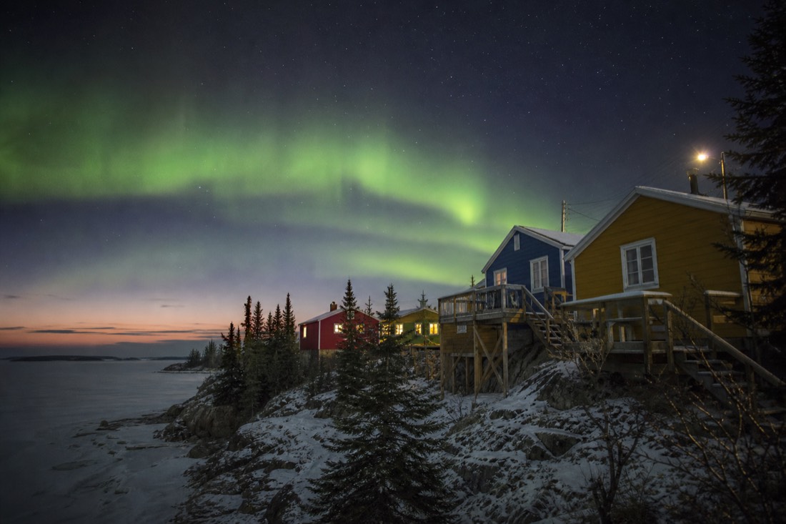 Colourful wooden shacks of Old Town Yellowknife on bare rock above a frozen bay at dusk