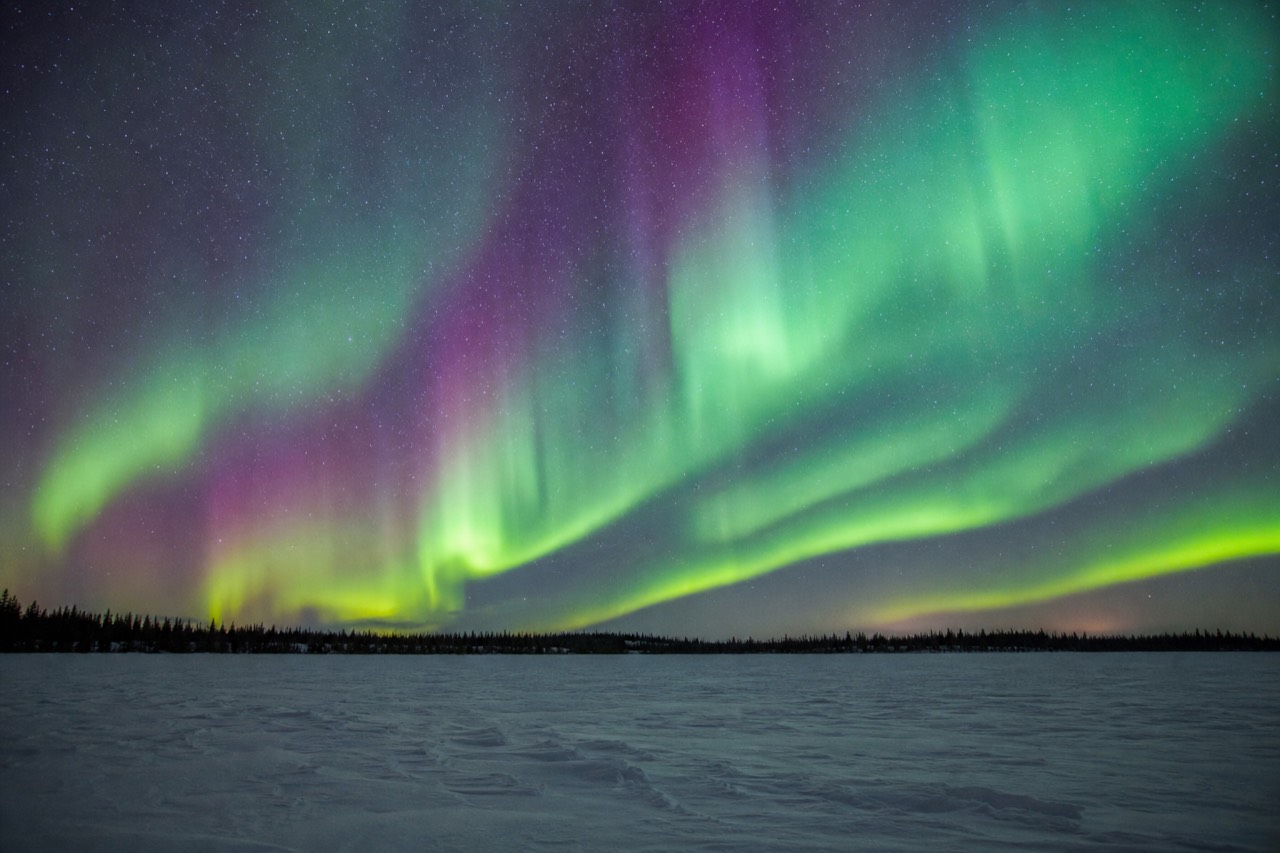 Strong green aurora arc filling the night sky over snow-covered lake ice near Yellowknife